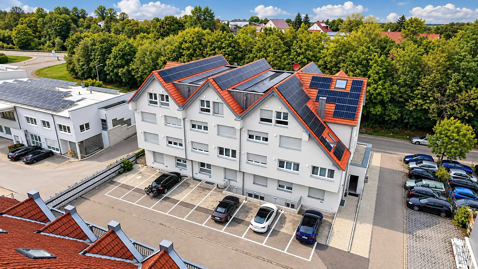 Luftaufnahme des SMARTHOTEL Aalen von hinten: weiß verputztes Gebäude mit roten Giebeldächern, darauf Photovoltaikmodule, davor markierte Stellplätze.