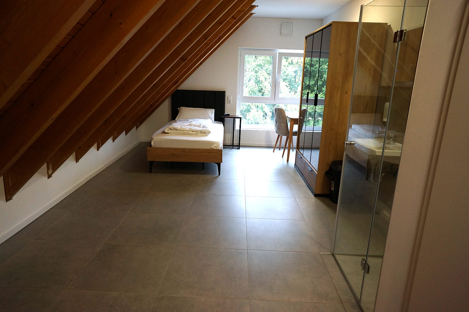 Budget Einzelzimmer unter der Dachschräge mit Einzelbett, Sitzecke am Fenster und offenem Bad hinter Glas.