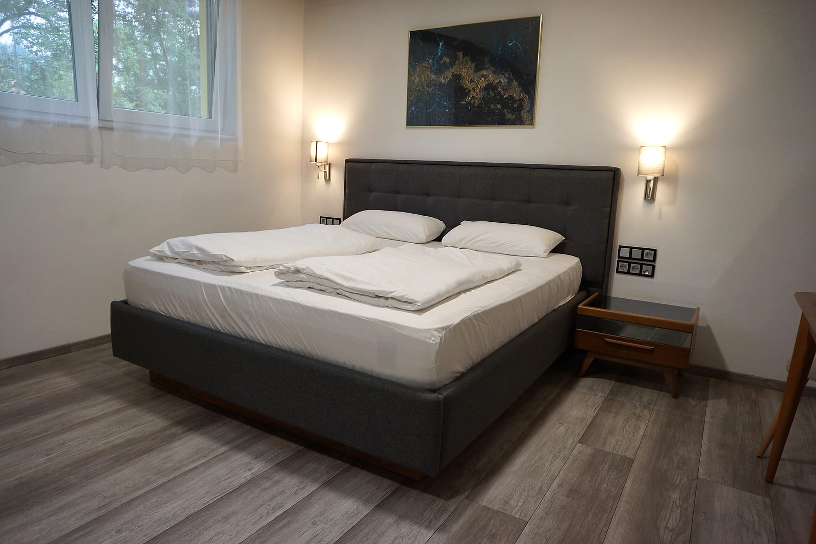 Studio Apartment mit großem Doppelbett, Wandleuchten und Nachttischen auf hellem Holzboden.